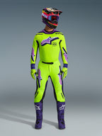 Pilota di motocross con maglia Alpinestars Supertech Vista 2026 giallo acceso con dettagli viola e neri, pantaloni gialli e viola coordinati, stivali viola, casco e guanti abbinati, set completo di abbigliamento professionale da gara