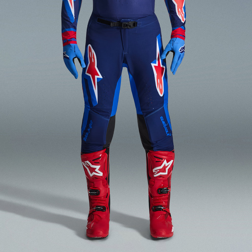 Alpinestars 2026 Supertech Vista Gear Set, pantaloni da motocross in blu navy e blu brillante con loghi rossi e bianchi, abbinati a guanti azzurri e stivali da motocross rosso acceso, abbigliamento da gara professionale.
