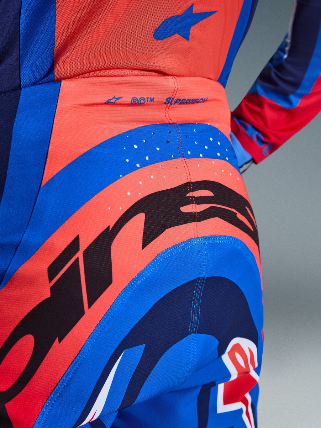 Alpinestars 2026 Supertech Vista Pants, pantaloni da motocross, blu navy scuro, hot coral e cobalto, vista posteriore ravvicinata con branding evidente, perforazioni tagliate al laser per la ventilazione e logo 'SUPERTECH' sulla fascia in vita, materiale elasticizzato ad alte prestazioni per gare fuoristrada