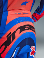 Dettaglio dei pantaloni Alpinestars Supertech Vista 2026, pantaloni da motocross, Hot Coral e blu cobalto, con una grande grafica Alpinestars nera sulla seduta, fori di ventilazione tagliati al laser e marchio 'SUPERTECH' sulla parte posteriore della vita, abbigliamento da gara professionale.