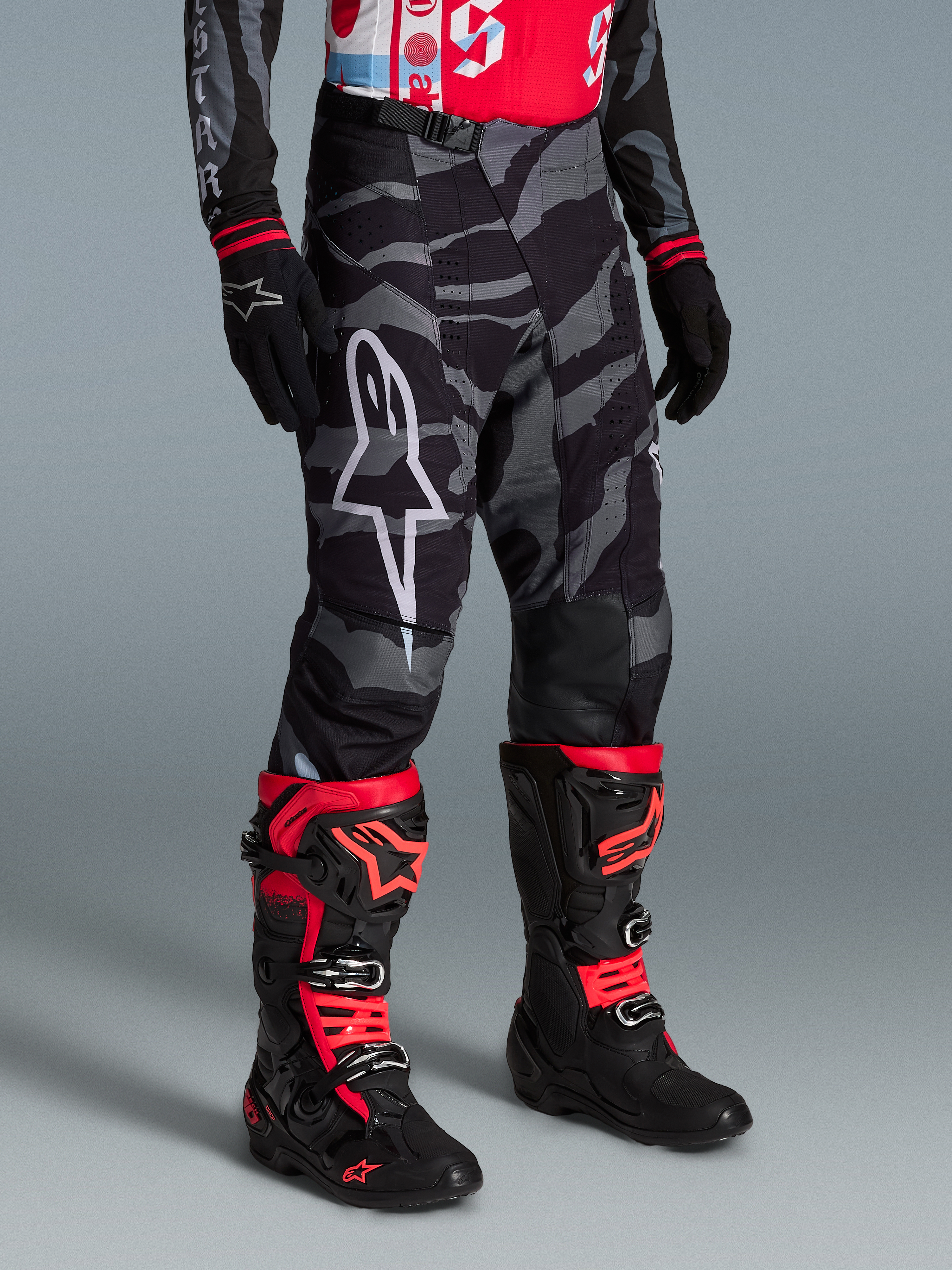Alpinestars Pantaloni Techstar Beast Coast Edizione Limitata, mimetici neri e grigi con stivali da motocross rossi e neri.