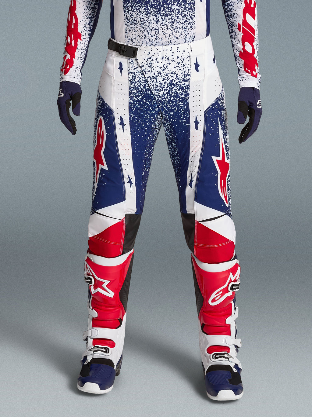 Alpinestars Completo Techstar Unity Edizione Limitata, pantaloni motocross macchiettati rossi, bianchi e blu con stivali.