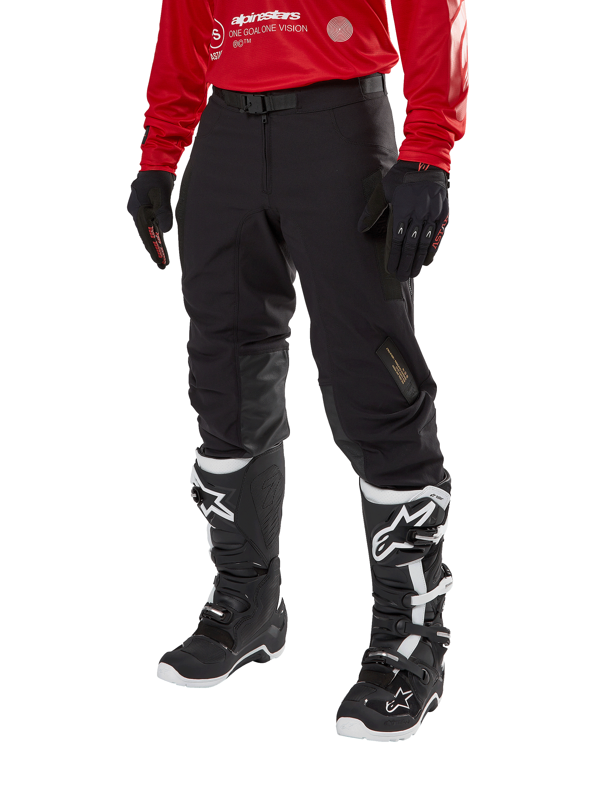 Alpinestars Techdura Pants, pantaloni da moto fuoristrada neri, indossati con una maglia rossa a maniche lunghe e stivali da motocross bianchi e neri, caratterizzati da una robusta costruzione in poliammide elasticizzata, rinforzi interni in pelle sulle ginocchia e cintura regolabile con fibbia per la guida enduro.