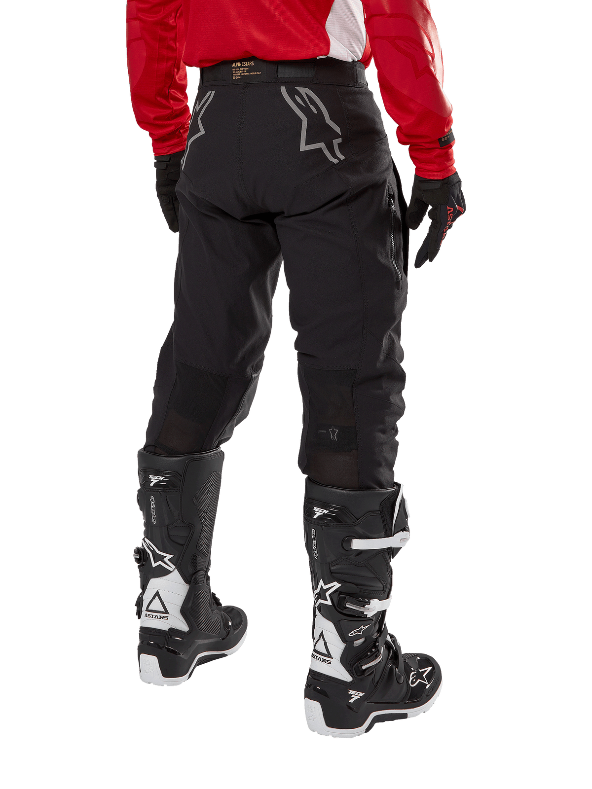 Pantaloni Alpinestars Techdura, pantaloni da enduro fuoristrada, nero, vista posteriore con loghi a stella grigi sulla seduta, indossati con maglia rossa a maniche lunghe e stivali Tech 7 neri e bianchi, robusta costruzione in tessuto per guida adventure