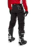 Pantaloni Alpinestars Techdura, pantaloni da enduro fuoristrada, nero, vista posteriore con loghi a stella grigi sulla seduta, indossati con maglia rossa a maniche lunghe e stivali Tech 7 neri e bianchi, robusta costruzione in tessuto per guida adventure