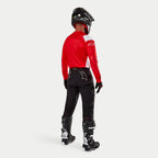 Pantaloni Alpinestars Techdura, pantaloni da enduro e off-road, nero, vista posteriore indossati da un pilota con maglia rossa e bianca e stivali neri e bianchi, con loghi a stella bianchi sul retro e costruzione tecnica elasticizzata resistente.