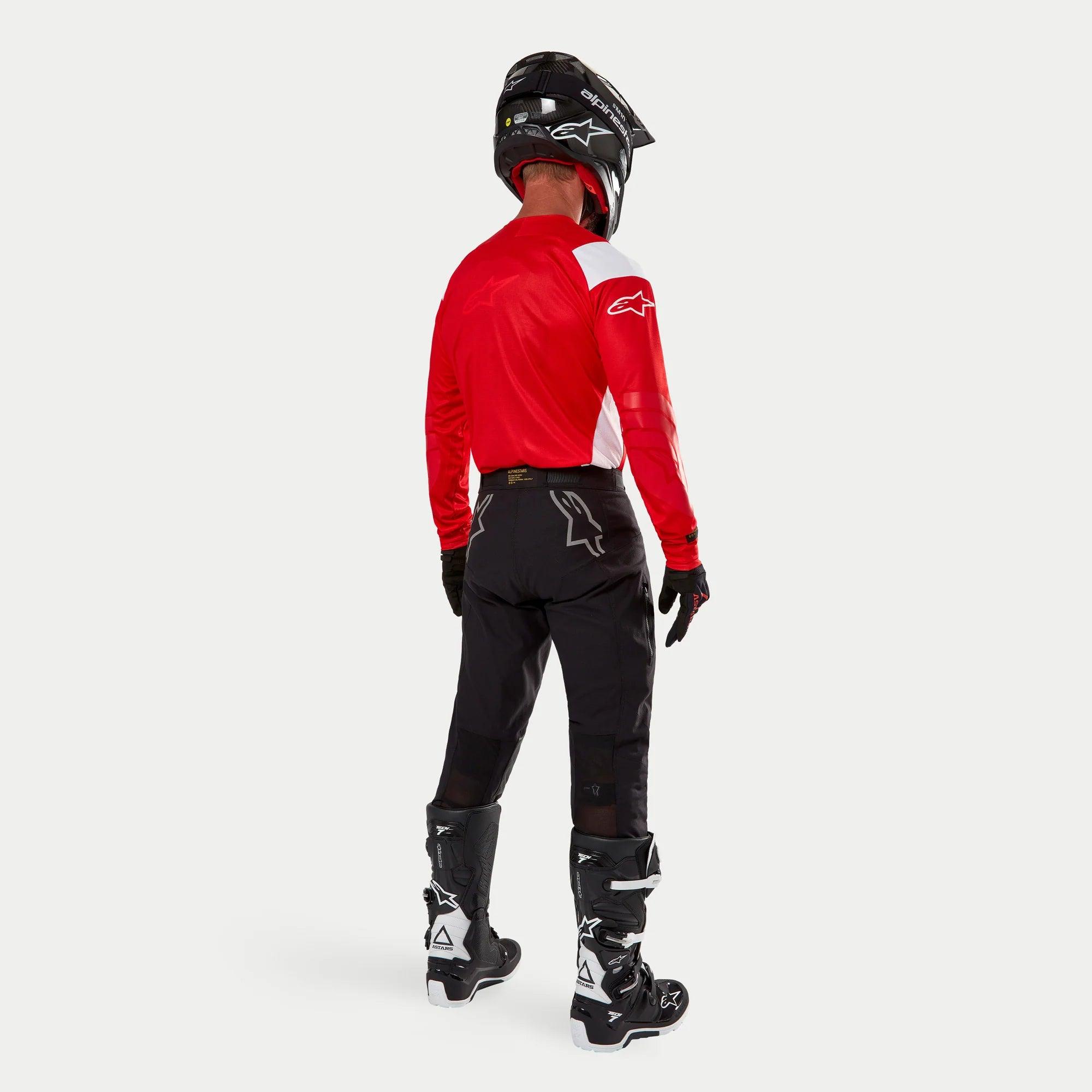 Pantaloni Alpinestars Techdura, pantaloni da enduro e off-road, nero, vista posteriore indossati da un pilota con maglia rossa e bianca e stivali neri e bianchi, con loghi a stella bianchi sul retro e costruzione tecnica elasticizzata resistente.