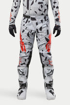 Alpinestars 2024 Techstar Rantera Pants, pantaloni da motocross, grigio mimetico Haze Gray, indossati con maglia coordinata, guanti neri e stivali bianchi, con motivo a macchie nere e logo Alpinestars rosso, design resistente per corse fuoristrada