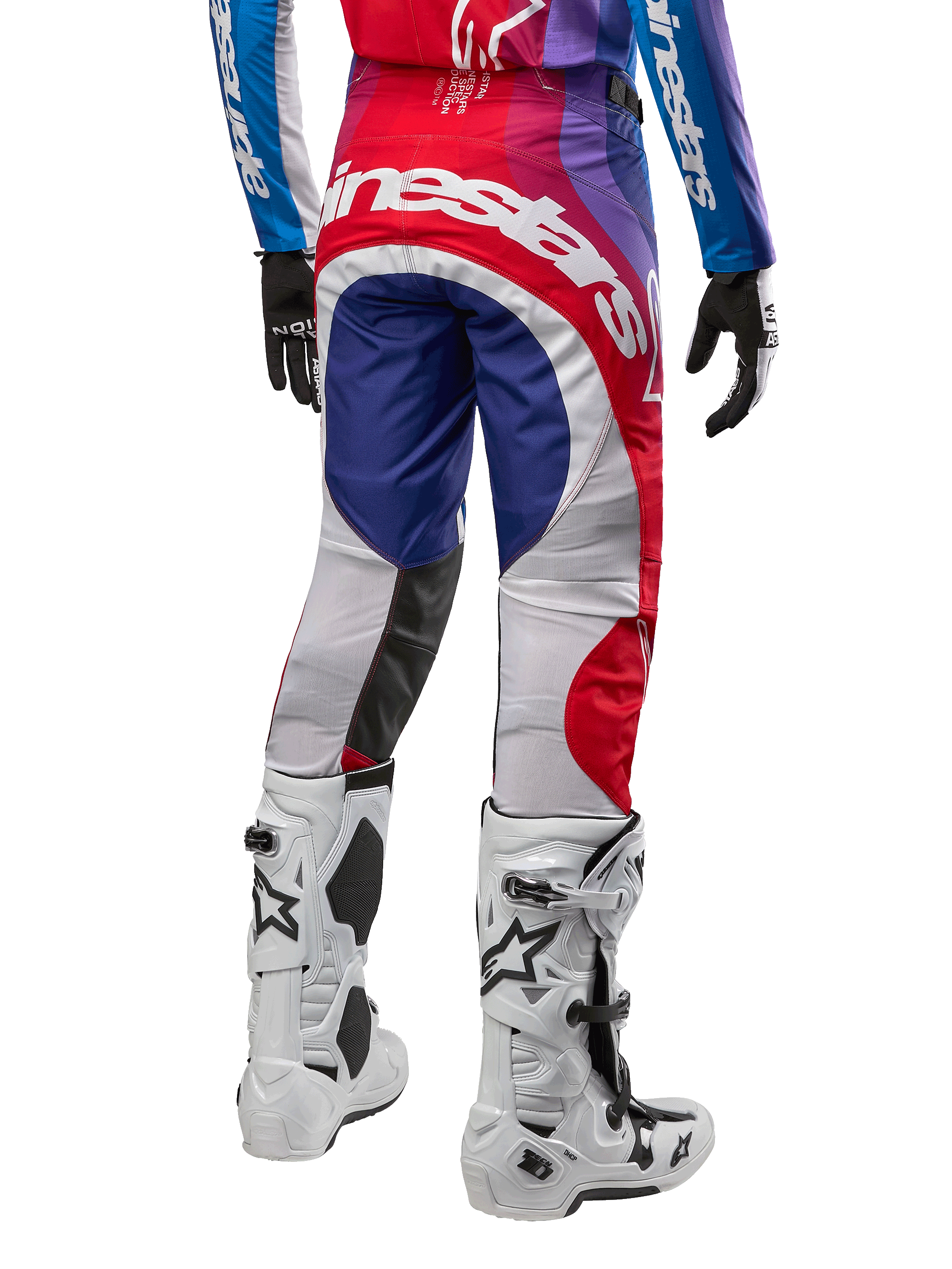 Alpinestars Pantaloni Techstar Pneuma 2024, pantaloni da motocross, Blu Mars Rosso Bianco, vista posteriore indossati con maglia coordinata e stivali bianchi, con logo bianco sulla seduta e pannelli multicolore, abbigliamento professionale da motocross