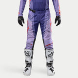 Alpinestars 2024 Techstar Ocuri Pants, pantaloni da motocross viola e arancione fluo, design tecnico con loghi rossi e pannelli traspiranti, indossati con stivali bianchi e guanti neri, equipaggiamento per fuoristrada