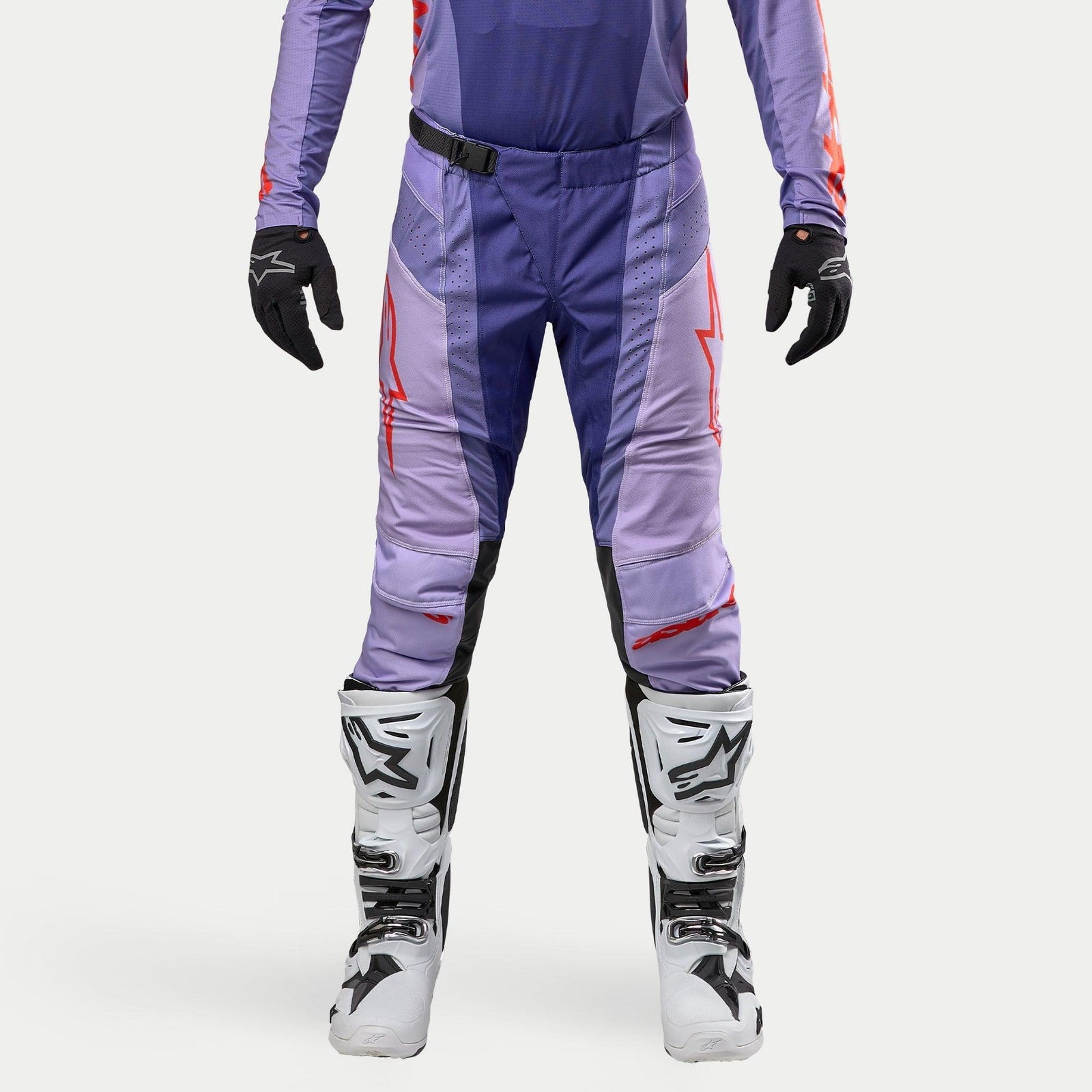 Alpinestars 2024 Techstar Ocuri Pants, pantaloni da motocross viola e arancione fluo, design tecnico con loghi rossi e pannelli traspiranti, indossati con stivali bianchi e guanti neri, equipaggiamento per fuoristrada