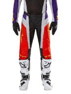 Alpinestars 2024 Techstar Ocuri Pants, pantaloni da motocross, arancione acceso, viola e nero, indossati con maglia coordinata, guanti neri e stivali bianchi, caratterizzati da pannelli anteriori arancione vivace, dettagli viola in vita e sezioni grigie traforate, design tecnico per corse off-road