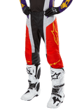 Alpinestars 2024 Techstar Ocuri Pants, pantaloni da motocross, arancione acceso, nero e bianco con grafica a stella gialla, indossati con maglia viola e stivali bianchi, abbigliamento tecnico resistente per competizioni fuoristrada
