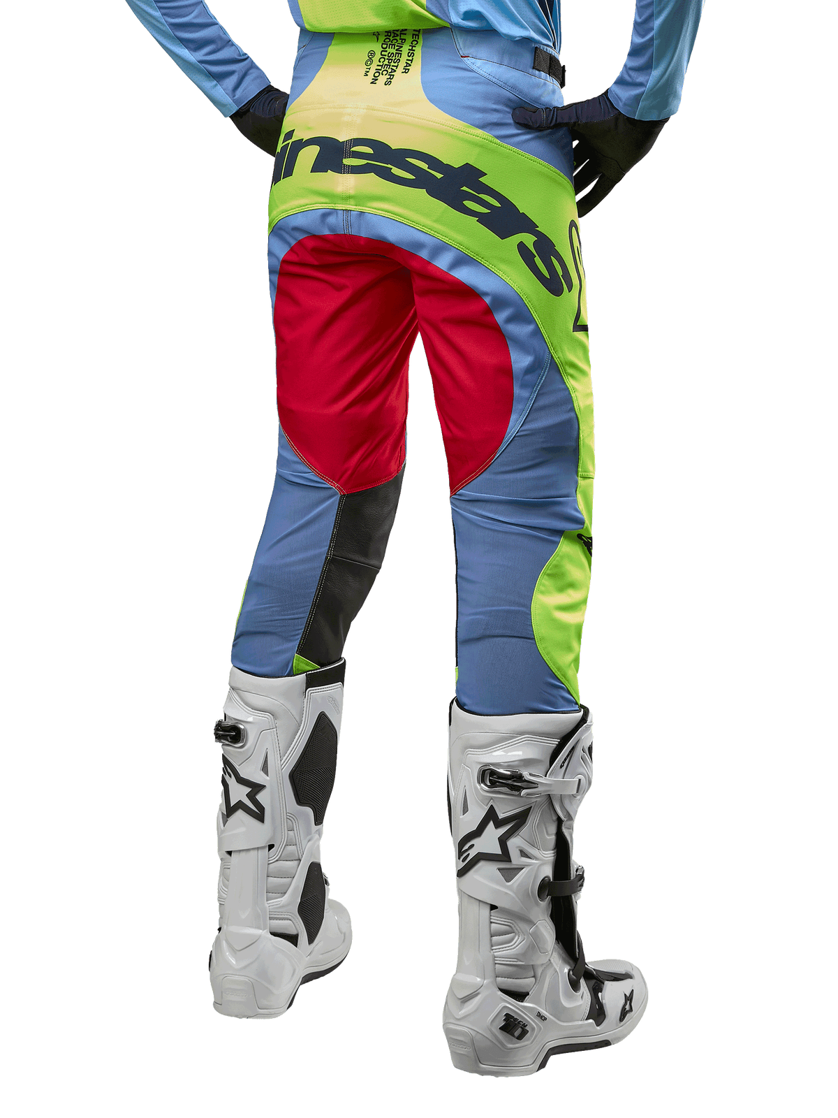 Alpinestars 2024 Techstar Ocuri Pants, pantaloni da motocross, celeste, giallo fluo e rosso berry, vista posteriore con stivali da motocross bianchi e neri, caratterizzati da vivaci blocchi di colore e vistoso marchio Alpinestars sulla seduta.
