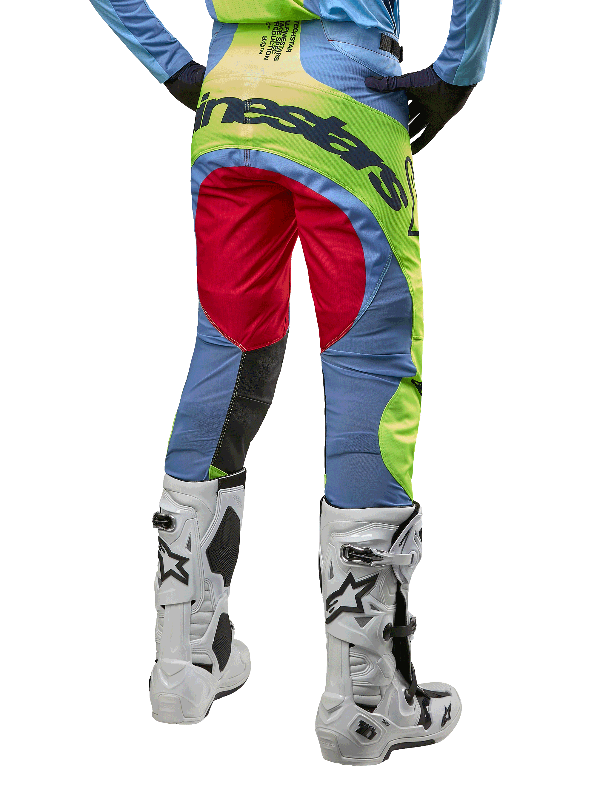 Alpinestars 2024 Techstar Ocuri Pants, pantaloni da motocross, celeste, giallo fluo e rosso berry, vista posteriore con stivali da motocross bianchi e neri, caratterizzati da vivaci blocchi di colore e vistoso marchio Alpinestars sulla seduta.