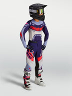 Alpinestars Supertech Dyna, pantaloni da motocross per ragazzi, viola e rosa fluo, in tessuto elasticizzato rip-stop, indossati da un giovane pilota in un completo da gara off-road