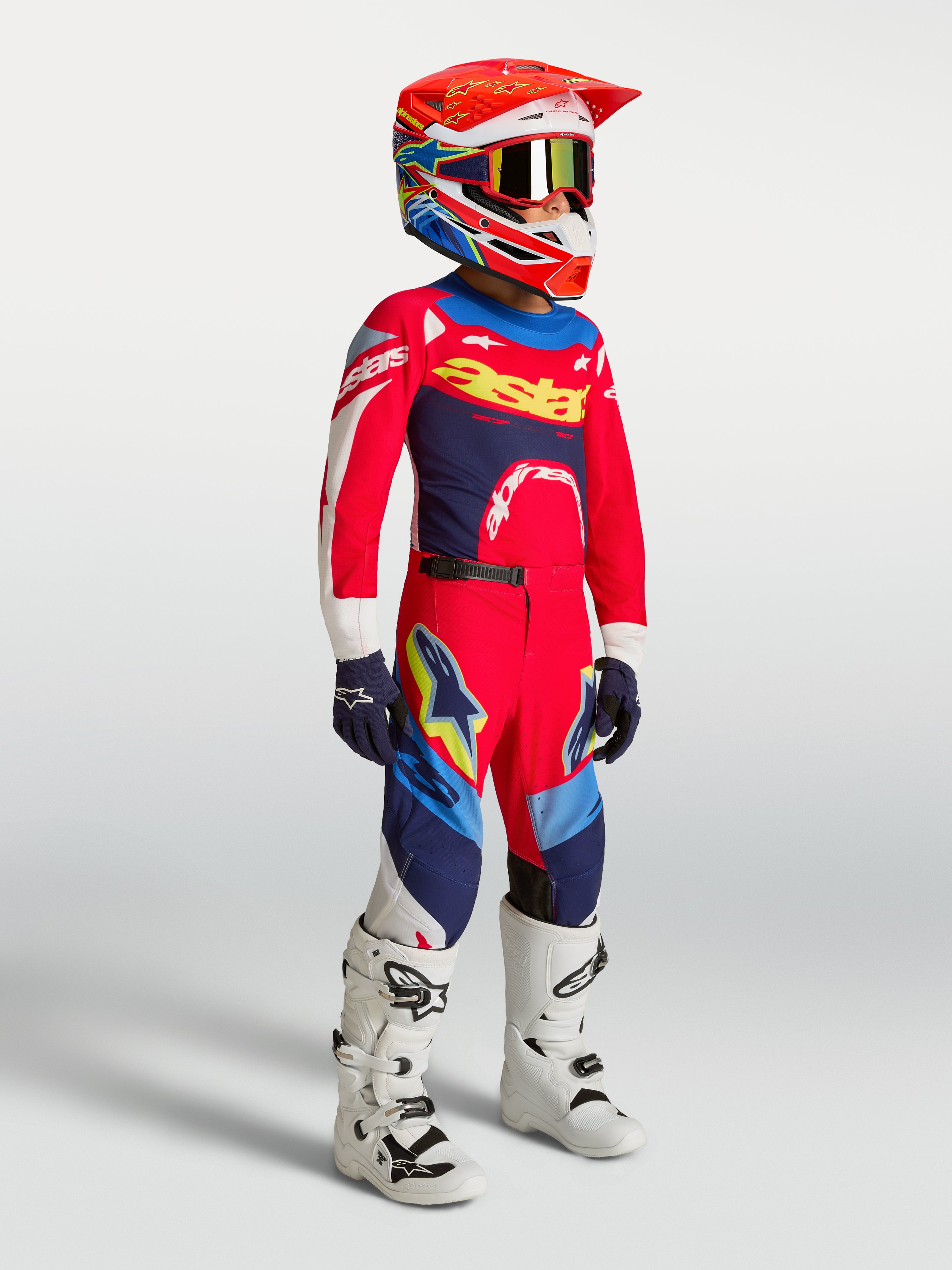 Alpinestars Pantaloni Supertech Dyna Ragazzo, abbigliamento da motocross per ragazzi, rosso e blu navy, indossati con maglia coordinata, casco e stivali bianchi