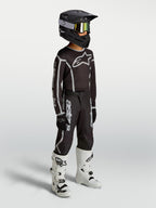 Alpinestars Pantaloni Fluid Apex V2 Ragazzo, pantaloni da motocross neri e argento con maglia, casco e stivali bianchi.