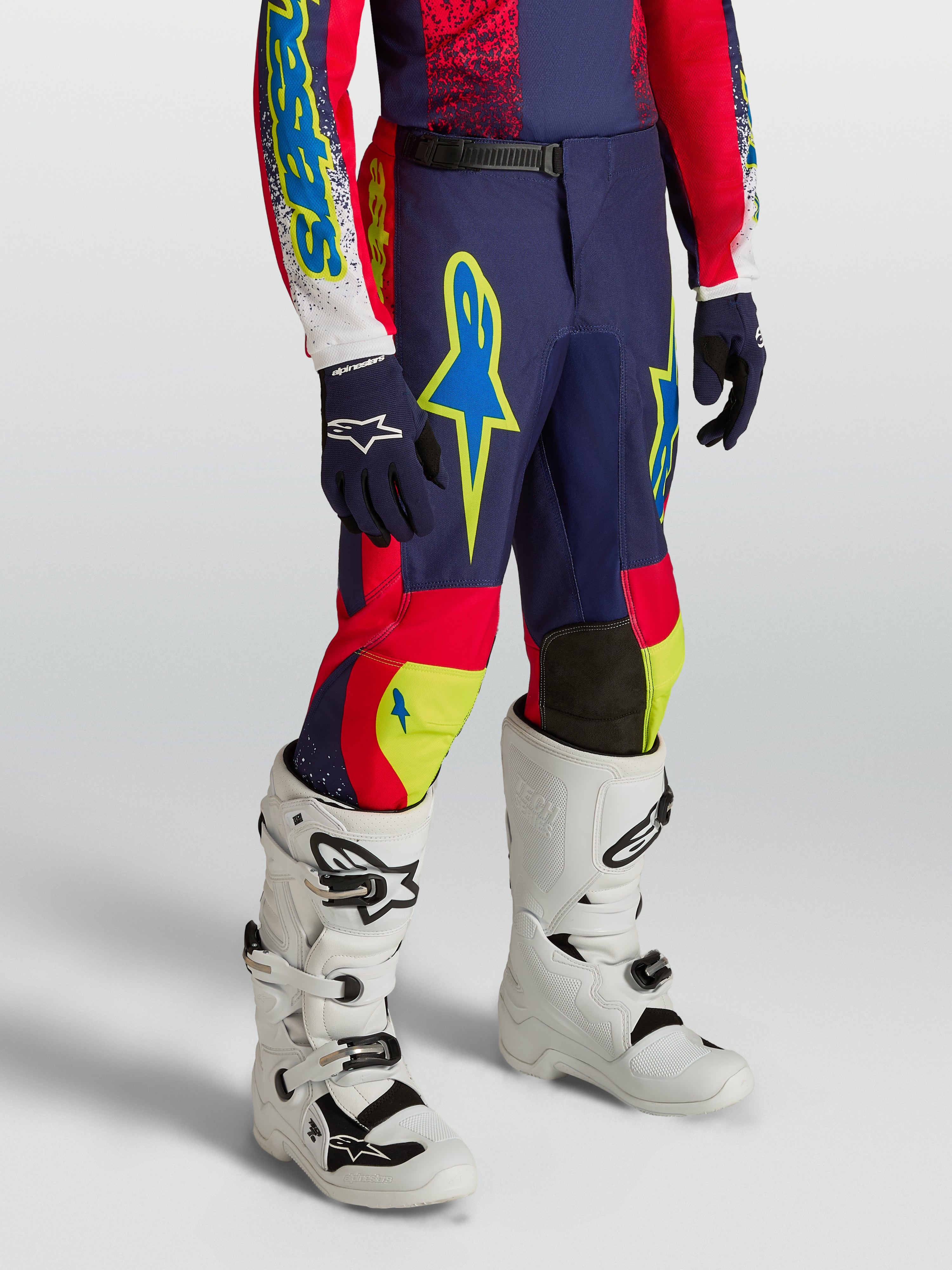 Alpinestars pantaloni Fluid Drag ragazzo 2027, completo motocross blu navy e rosso con dettagli neon e stivali bianchi.