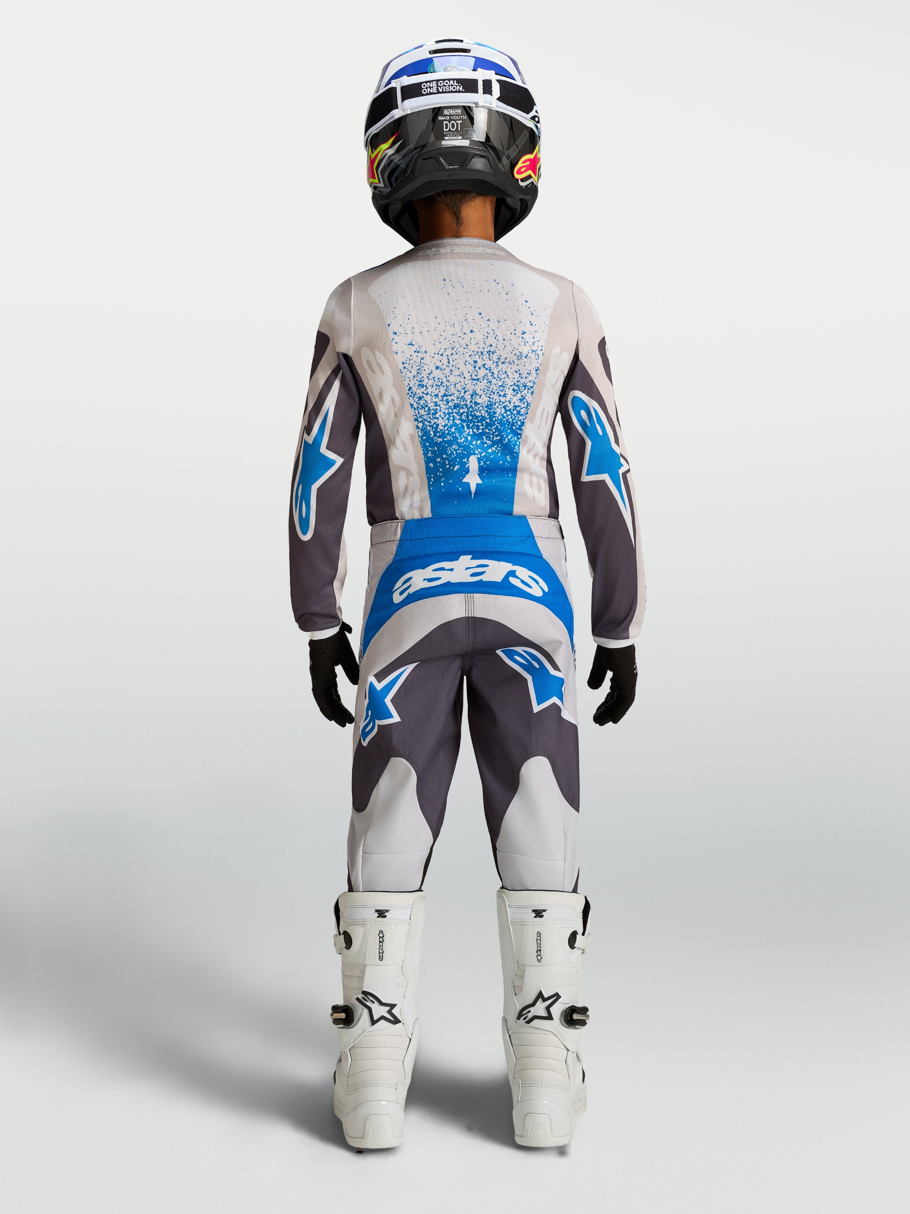 Alpinestars Pantaloni Fluid Drag Ragazzo, pantaloni motocross grigio e blu, vista posteriore con maglia e stivali coordinati.