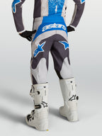 Alpinestars Pantaloni Fluid Drag Ragazzo, pantaloni da motocross grigi e blu, visti da dietro su un pilota con stivali bianchi, abbigliamento tecnico off-road.