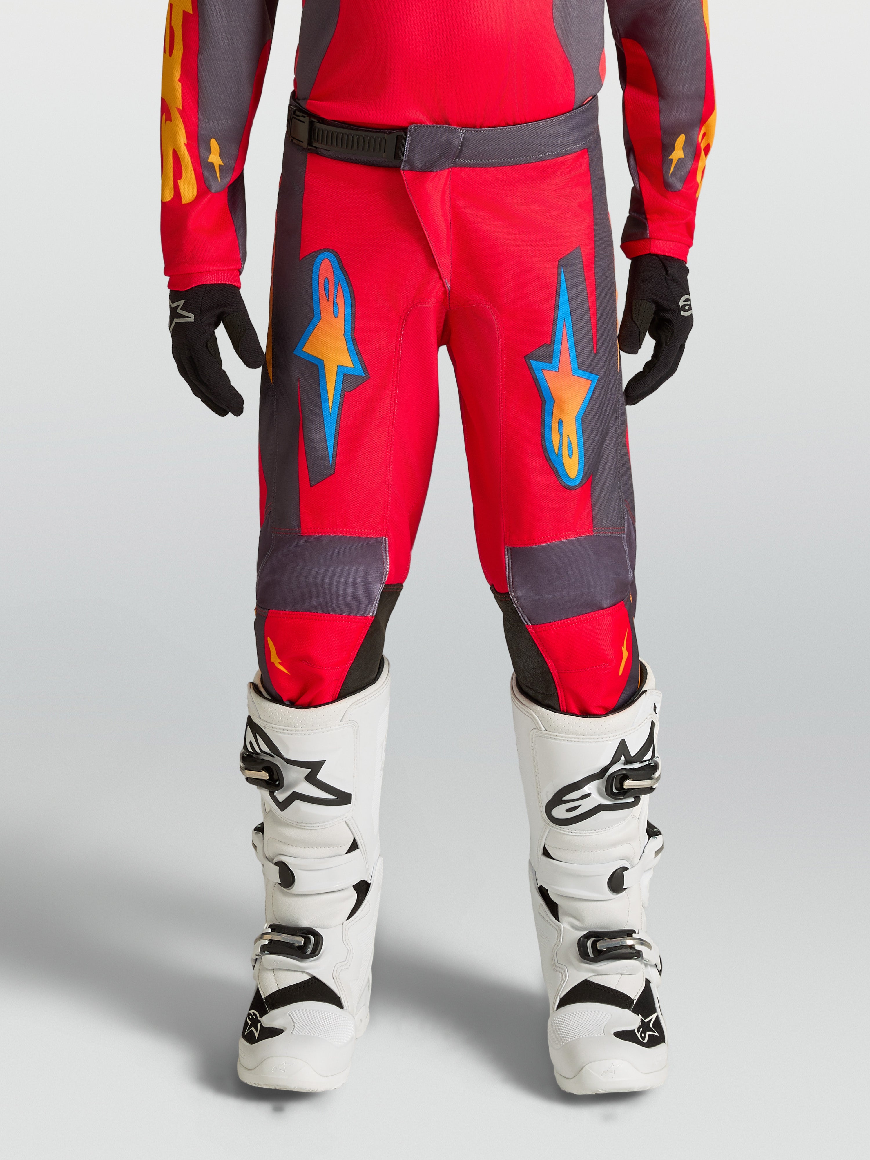 Alpinestars Pantaloni Fluid Hunt Ragazzo, pantaloni da motocross rossi e grigi per guida off-road, design ergonomico in tessuto poliestere con grafiche blu e arancioni, abbigliamento tecnico per giovani piloti.