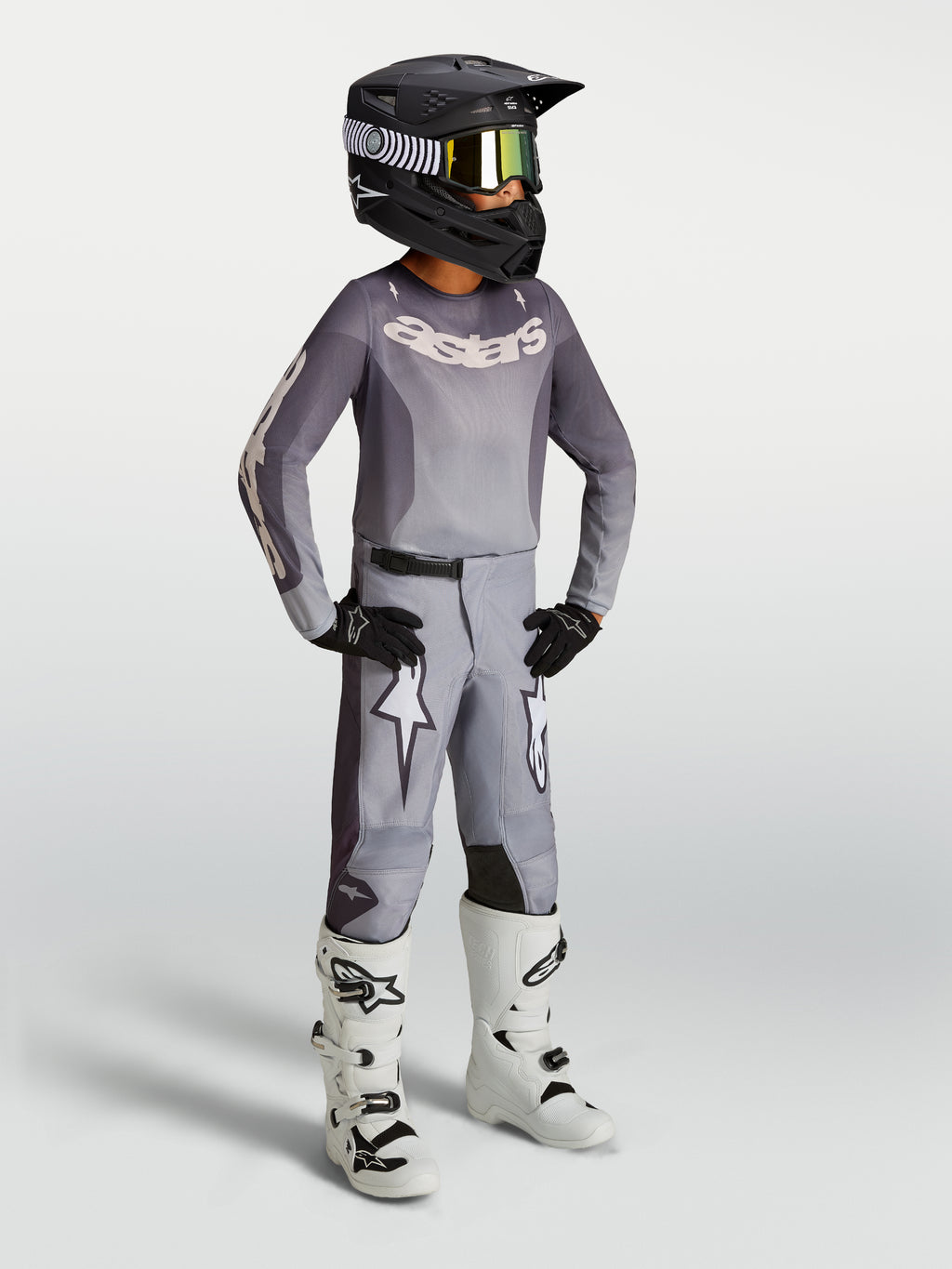 Alpinestars Pantaloni Fluid Amber Ragazzo 2027, pantaloni da motocross per ragazzi, colore sabbia e grigio con grafiche a stella bianche, vestibilità sportiva pre-curvata, rinforzati per off-road, indossati con casco nero e stivali bianchi
