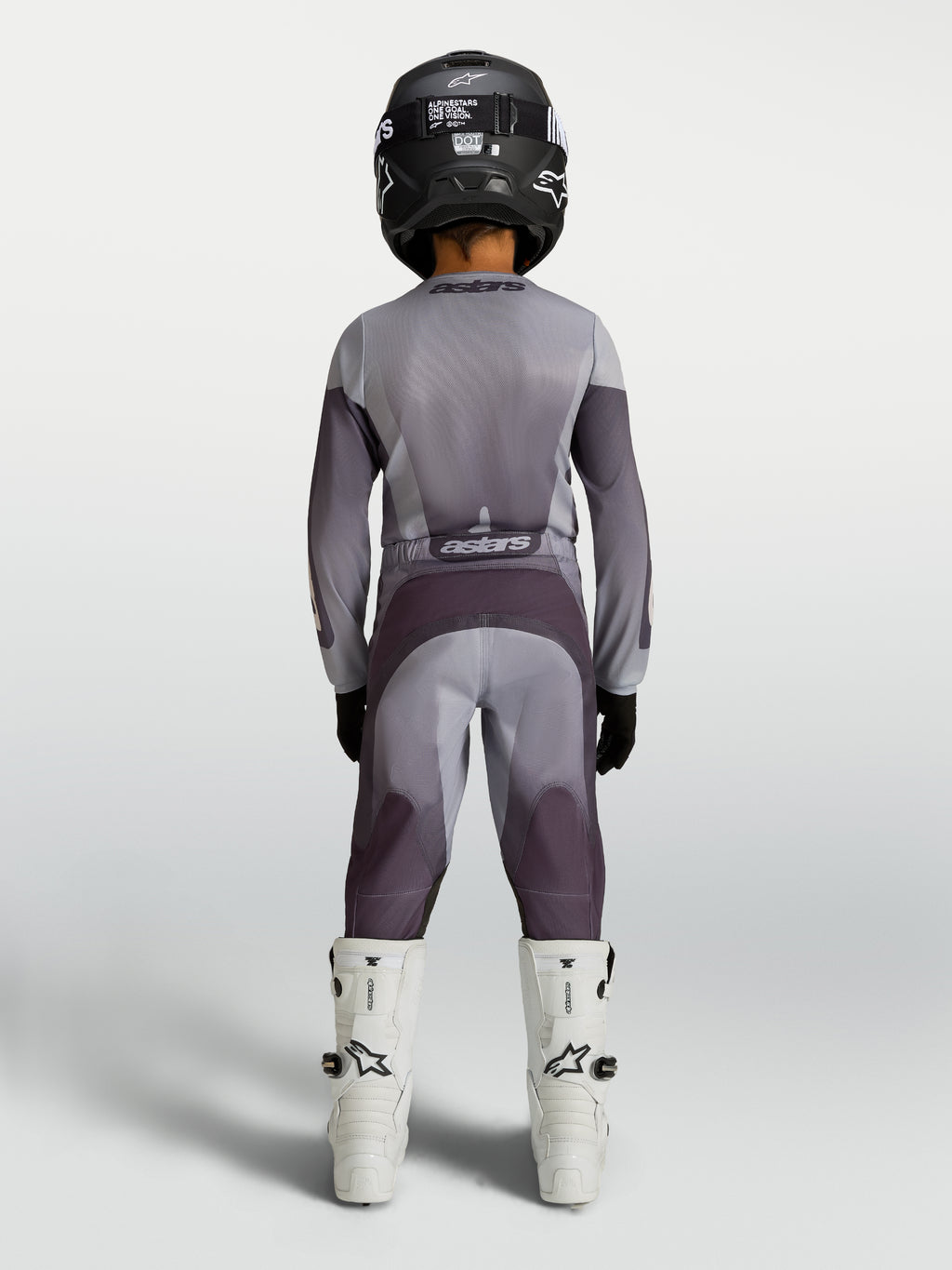 Alpinestars Pantaloni Fluid Amber Ragazzo 2027, pantaloni da motocross per ragazzi, grigio e sabbia, vista posteriore su un pilota, abbigliamento fuoristrada resistente e protettivo.