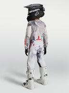 Alpinestars Pantaloni Fluid Lone Ragazzo, pantaloni motocross grigio mimetico e bianchi con dettagli rossi, indossati da un giovane pilota visto da dietro