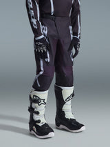 Alpinestars Pantaloni Youth Fluid Apex 2026, pantaloni da motocross, nero e grigio, con logo bianco evidente, indossati con maglia coordinata, guanti neri e bianchi e stivali bianchi e neri, equipaggiamento professionale da corsa fuoristrada