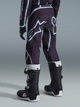Pantaloni Alpinestars Fluid Apex Ragazzo 2026, pantaloni da motocross, nero e grigio, indossati con maglia coordinata e stivali bianchi e neri, con grandi loghi A-star bianchi sulla seduta e sulle gambe, design sportivo ed ergonomico per prestazioni fuoristrada.