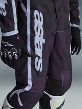 Alpinestars Pantaloni Youth Fluid Apex 2026, pantaloni da motocross, nero e grigio, vista ravvicinata del marchio 'astars' bianco sulla gamba, abbinati a guanti e stivali bianchi e neri, design sportivo per gare fuoristrada giovanili