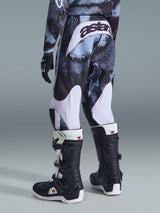 Alpinestars 2026 Youth Fluid Lahnd Pants, pantaloni da motocross, Iron Camo con accenti bianchi, vista posteriore con marchio 'astars' sulla seduta, indossati con maglia camo coordinata e stivali da motocross Tech 3 neri e bianchi