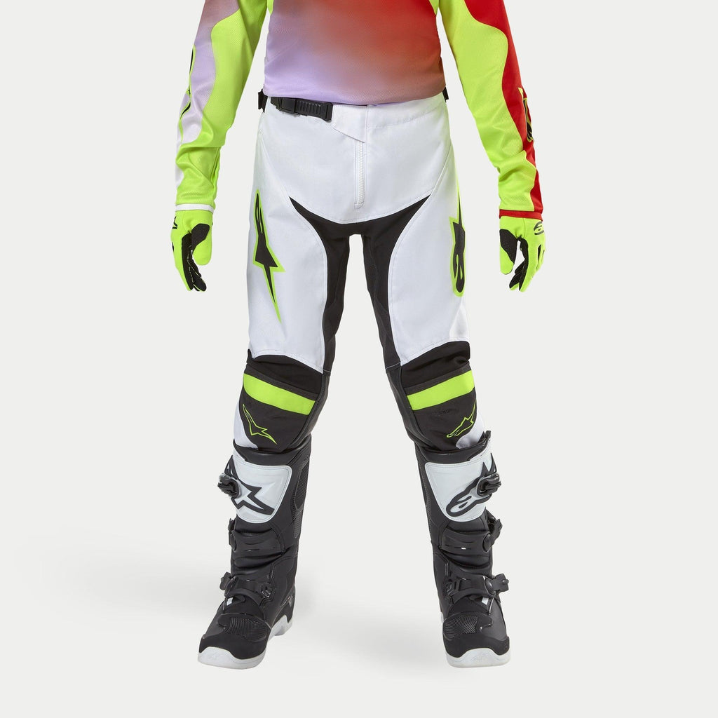 Alpinestars pantaloni Youth Racer Lucent 2024, pantaloni da motocross, bianco con accenti giallo neon e nero, indossati con guanti neon coordinati e stivali neri, con gambe pre-curvate ergonomiche e loghi Alpinestars, equipaggiamento ad alte prestazioni per corse fuoristrada