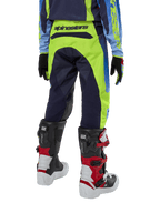 Alpinestars Youth 2024 Racer Hoen Pants, pantaloni da motocross, giallo fluo e blu night navy, vista posteriore con evidente marchio Alpinestars sulla fascia in vita, indossati con stivali Tech Series neri e rossi e maglia coordinata, vestibilità sportiva per fuoristrada ragazzi