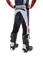 Alpinestars pantaloni Youth 2024 Racer Hoen, pantaloni da motocross, grigio chiaro con accenti arancione acceso e nero, vista posteriore con pannelli neri sulla seduta e sulle gambe, branding evidente sulla vita posteriore, indossati con stivali da motocross bianchi e neri per corse fuoristrada