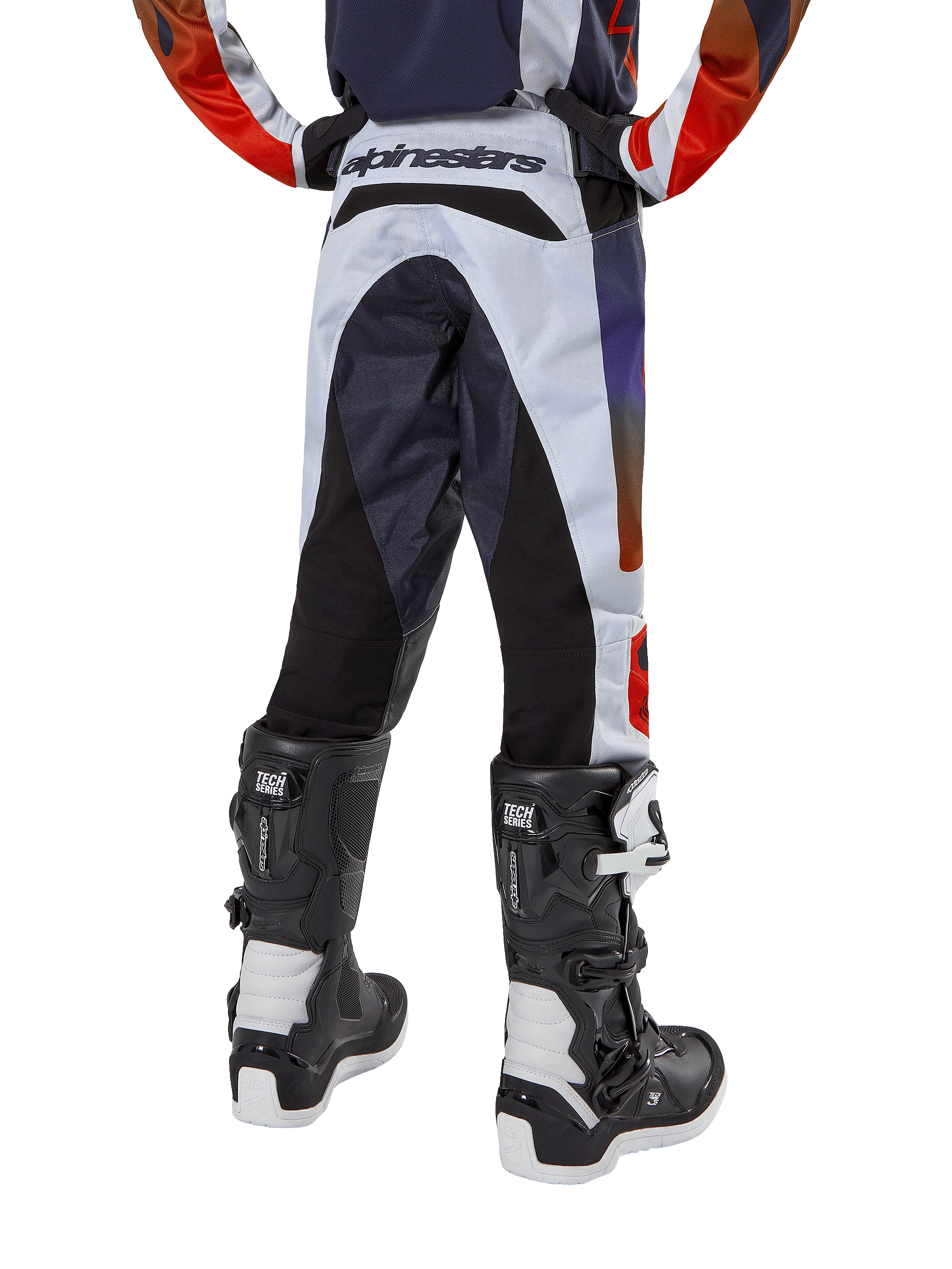 Alpinestars pantaloni Youth 2024 Racer Hoen, pantaloni da motocross, grigio chiaro con accenti arancione acceso e nero, vista posteriore con pannelli neri sulla seduta e sulle gambe, branding evidente sulla vita posteriore, indossati con stivali da motocross bianchi e neri per corse fuoristrada