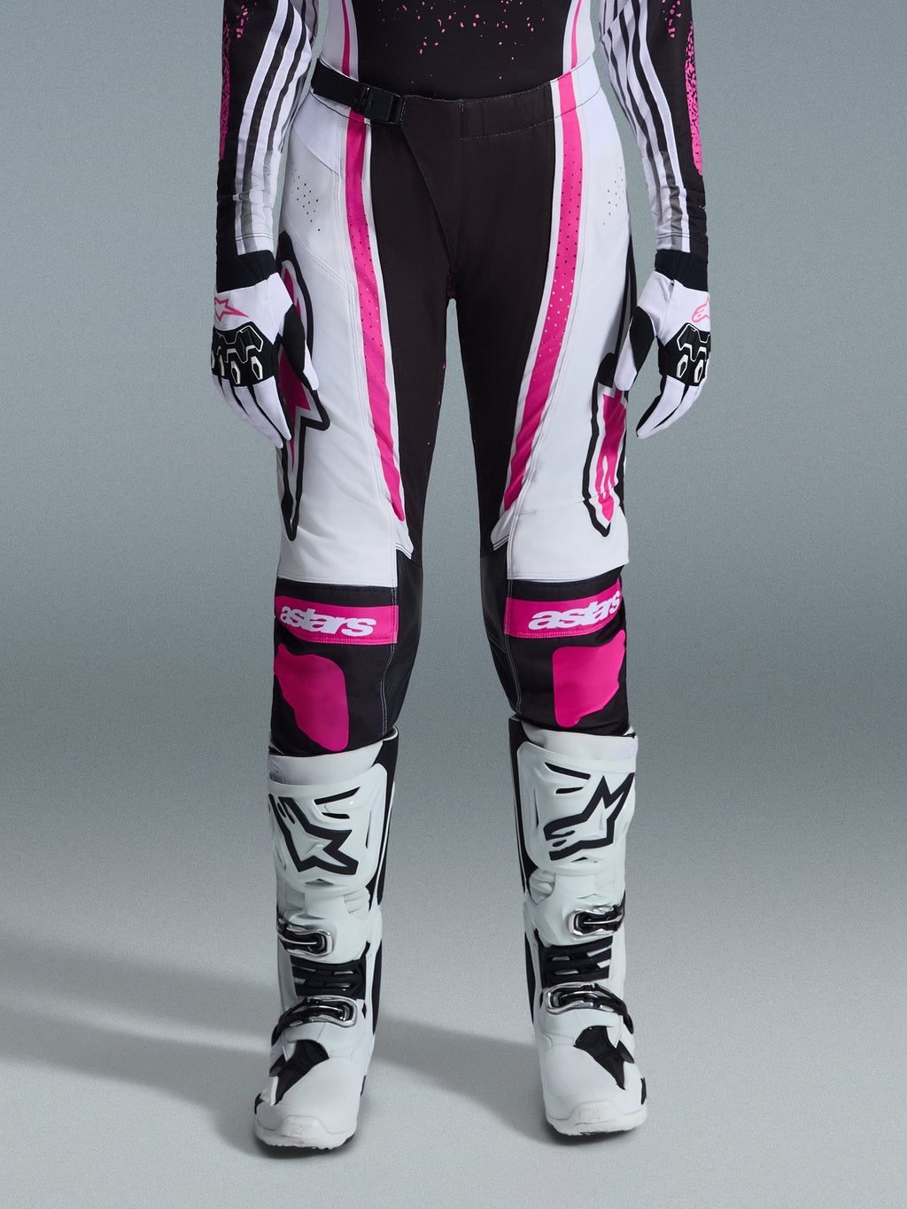 Pantaloni Alpinestars 2026 Stella Techstar Nomur Donna, pantaloni da motocross, nero, bianco e fucsia, indossati con maglia da gara coordinata, guanti e stivali da motocross bianchi, caratterizzati da audaci grafiche rosa e loghi astars sulle ginocchia, progettati per competizioni fuoristrada di alto livello.