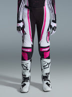 Pantaloni Alpinestars 2026 Stella Techstar Nomur Donna, pantaloni da motocross, nero, bianco e fucsia, indossati con maglia da gara coordinata, guanti e stivali da motocross bianchi, caratterizzati da audaci grafiche rosa e loghi astars sulle ginocchia, progettati per competizioni fuoristrada di alto livello.