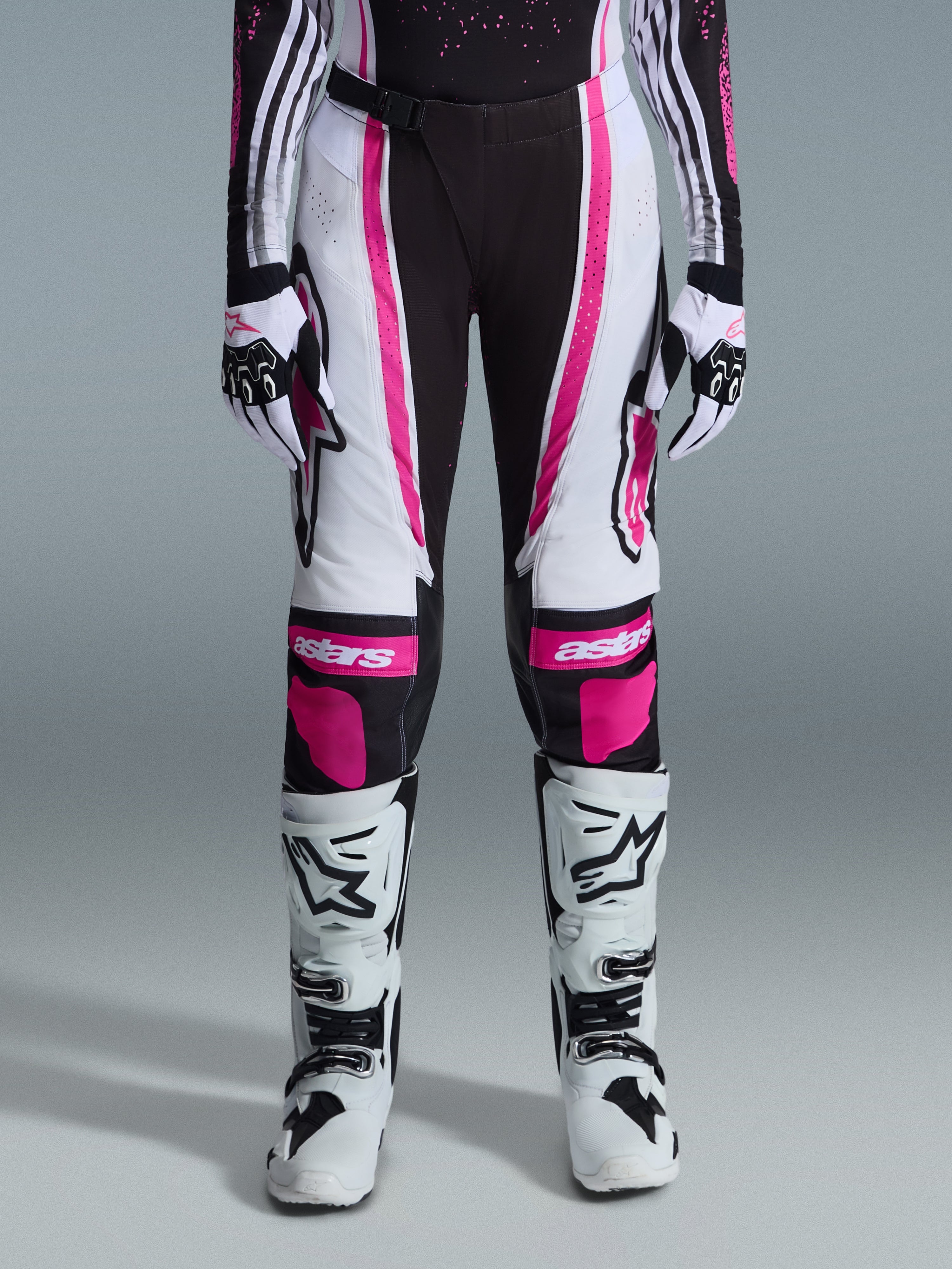 Pantaloni Alpinestars 2026 Stella Techstar Nomur Donna, pantaloni da motocross, nero, bianco e fucsia, indossati con maglia da gara coordinata, guanti e stivali da motocross bianchi, caratterizzati da audaci grafiche rosa e loghi astars sulle ginocchia, progettati per competizioni fuoristrada di alto livello.