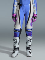 Alpinestars Stella Techstar Nomur Donna 2026, pantaloni da motocross, azzurro, bianco sporco e nero, abbinati a stivali da motocross bianchi e guanti rosa e neri, con marchio 'astars' sulle ginocchia e design tecnico multi-pannello per motocicliste.