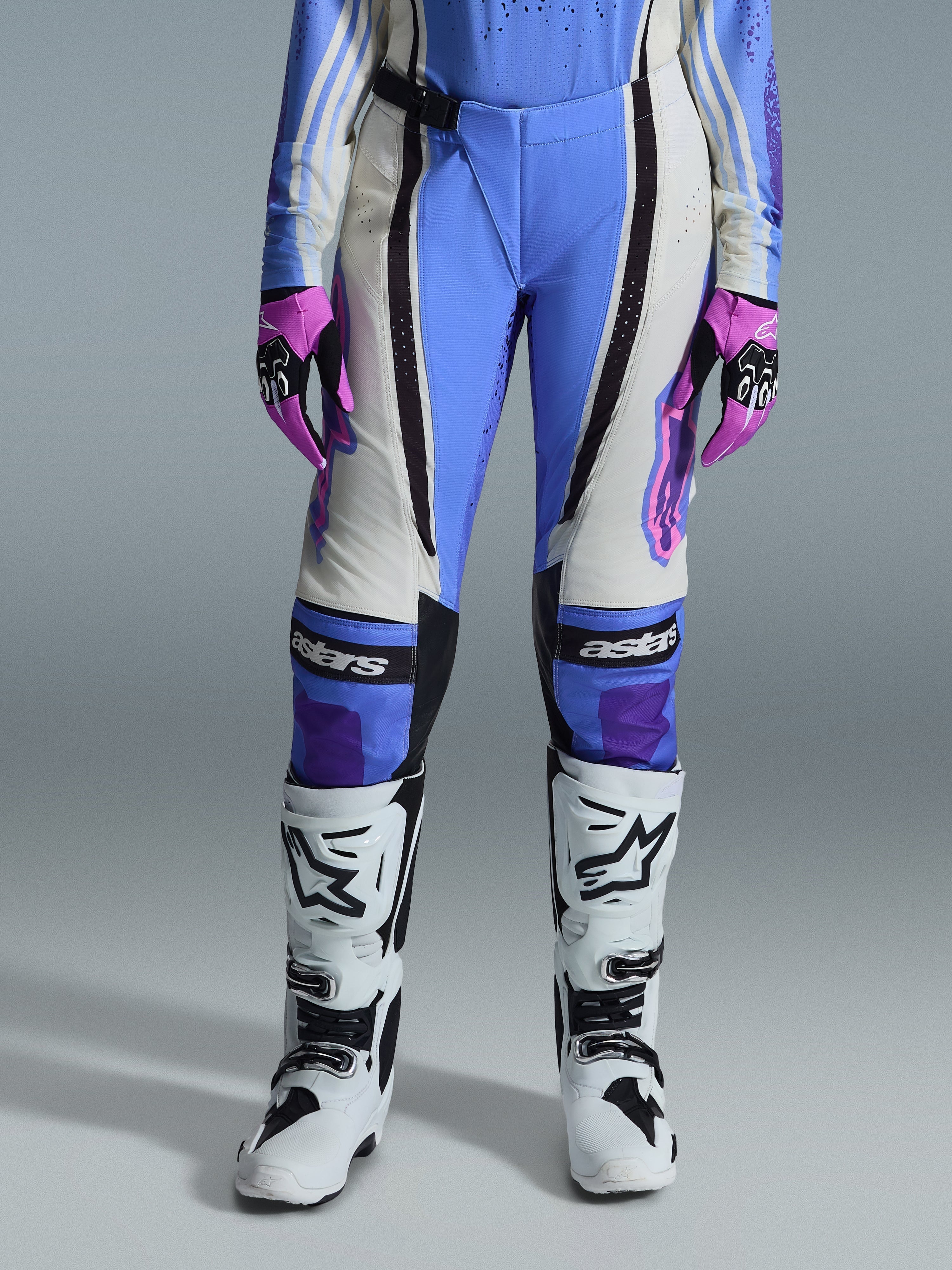 Alpinestars Stella Techstar Nomur Donna 2026, pantaloni da motocross, azzurro, bianco sporco e nero, abbinati a stivali da motocross bianchi e guanti rosa e neri, con marchio 'astars' sulle ginocchia e design tecnico multi-pannello per motocicliste.