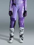 Alpinestars Stella Fluid Apex 2026 da donna, pantaloni da motocross, viola e bianco, indossati con guanti neri e viola e stivali bianchi e neri, con vistoso logo bianco sulla gamba, design ergonomico sport-fit per corse fuoristrada