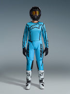 Alpinestars Stella Fluid Apex Gear Set 2026, maglia e pantaloni da motocross da donna, blu e nero, con grande logo a stella sul petto, indossato con casco nero, occhiali con lenti colorate e stivali bianchi con dettagli neri, completo da gara fuoristrada