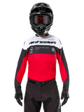 Maglia Alpinestars Pro-Dura, maglia da motocross, nero, rosso acceso e bianco, indossata con casco e occhiali neri, design sportivo con logo Alpinestars in evidenza e traforatura laser, abbigliamento tecnico per enduro e corse off-road