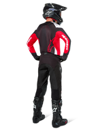 Pilota di motocross visto da dietro con maglia Alpinestars Pro-Dura in nero, rosso acceso e bianco, abbinata a pantaloni, casco e stivali neri, mostra il design posteriore e i loghi sulle maniche, abbigliamento coordinato per corse off-road.