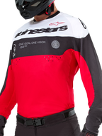 Maglia Alpinestars Pro-Dura, maglia da motocross ed enduro, nero, rosso brillante e bianco, con grafica 'ONE GOAL. ONE VISION.' e perforazioni laser sul petto, indossata con pantaloni da motocross neri e casco