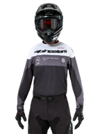 Pilota di motocross con maglia Alpinestars Pro-Dura in Black Magnet White, maglia tecnica a maniche lunghe con inserti bianchi e grigi, indossata con casco e occhiali neri, con logo 'alpinestars' e slogan 'ONE GOAL ONE VISION', abbigliamento da moto off-road