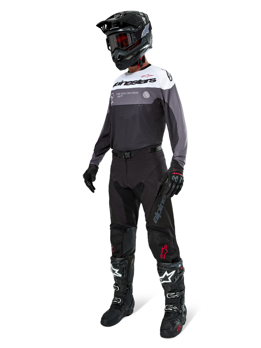 Maglia Alpinestars Pro-Dura in Black Magnet White, indossata da un pilota di motocross con equipaggiamento completo che include pantaloni neri, casco nero con occhiali e stivali bianchi e neri. La maglia presenta un design tecnico color-block con pannelli bianchi, grigi e neri, studiata per prestazioni enduro e off-road.