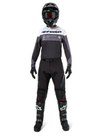 Pilota di motocross con equipaggiamento da gara completo, maglia Pro-Dura in Black Magnet White con parte superiore del petto bianca e dettagli grigi, abbinata a pantaloni neri, casco nero con maschera scura, stivali bianchi e neri e guanti neri, outfit coordinato per enduro e fuoristrada